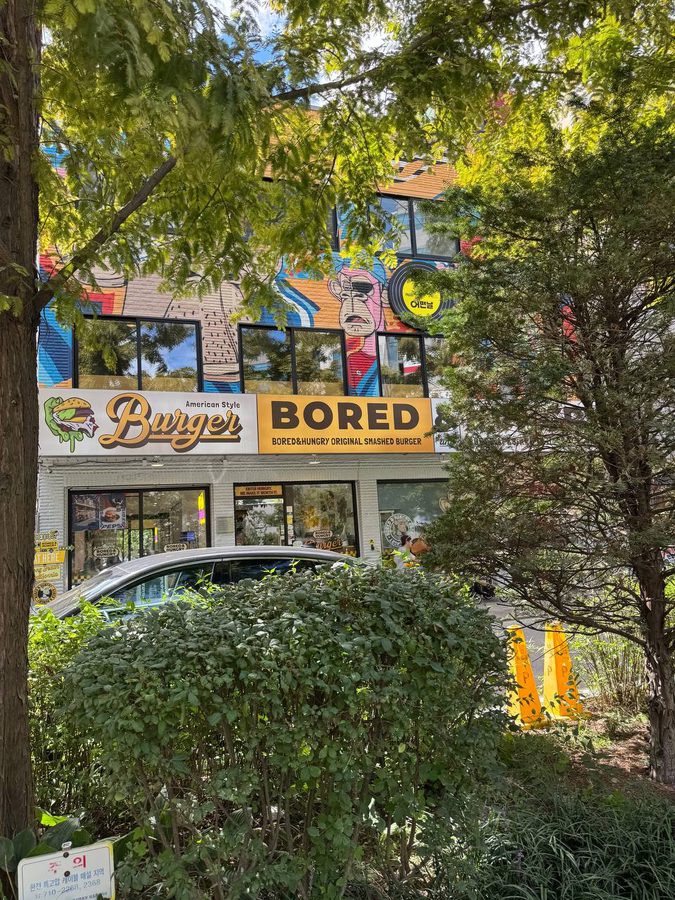 나뭇가지 사이로 보이는 American Style Burger, BORED 간판과 건물 위쪽의 알록달록한 벽화
