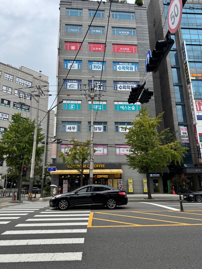 대흥역 사거리 건물 외벽에 수학학원, 국어학원, 논술학원 간판이 층마다 나란히 붙어 있고 1층에는 컴포즈커피가 있는 모습