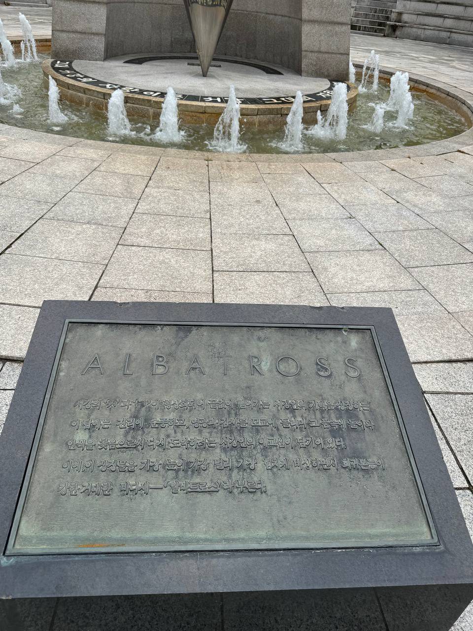 분수대 앞 검은 받침 위의 ALBATROSS 동판, 녹이 슨 표면에 탑의 의미를 설명하는 한글 문장이 새겨져 있다