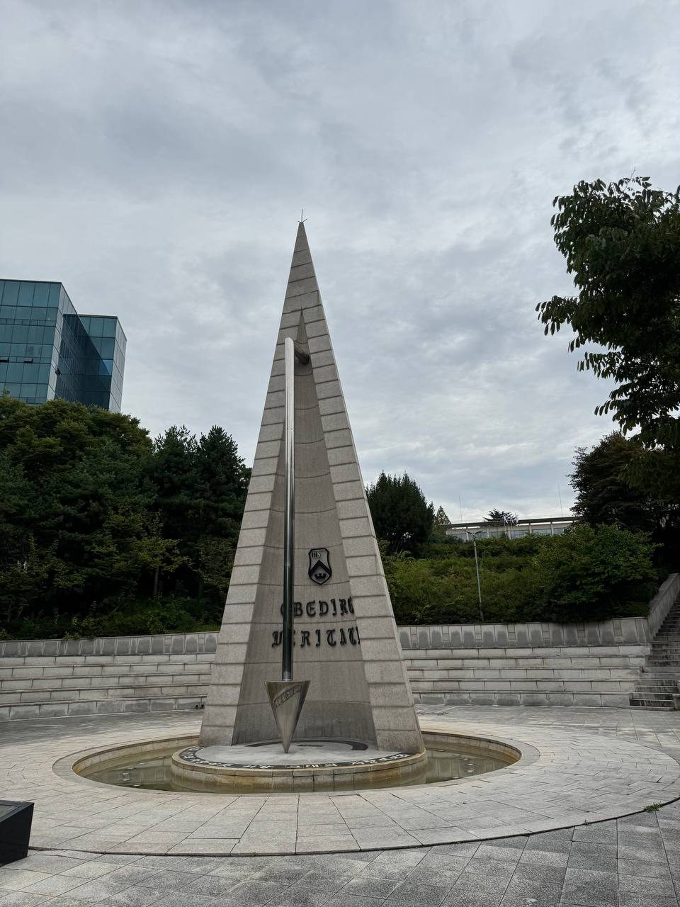 비스듬한 각도에서 본 알바트로스 탑, 왼쪽 뒤로 푸른 유리 외벽 건물이 보이고 오른쪽에는 석단 위로 계단이 이어진다