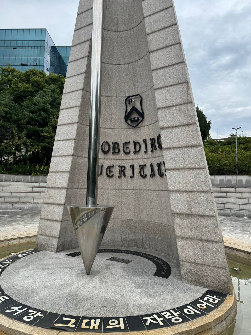 비스듬한 각도에서 가까이 찍은 교표와 OBEDIRE VERITATI, 매끈한 역원뿔 추 표면에 바닥 글씨가 비쳐 보인다