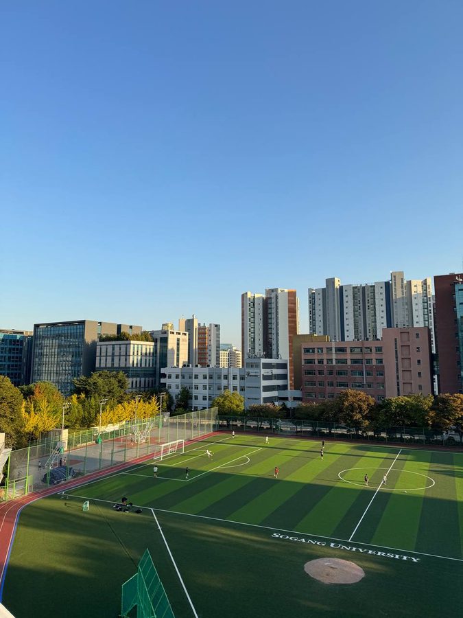 맑고 푸른 하늘 아래 서강대 운동장과 교내 건물들이 보이고, 운동장 가장자리 나무들이 노랗게 물들어 있다