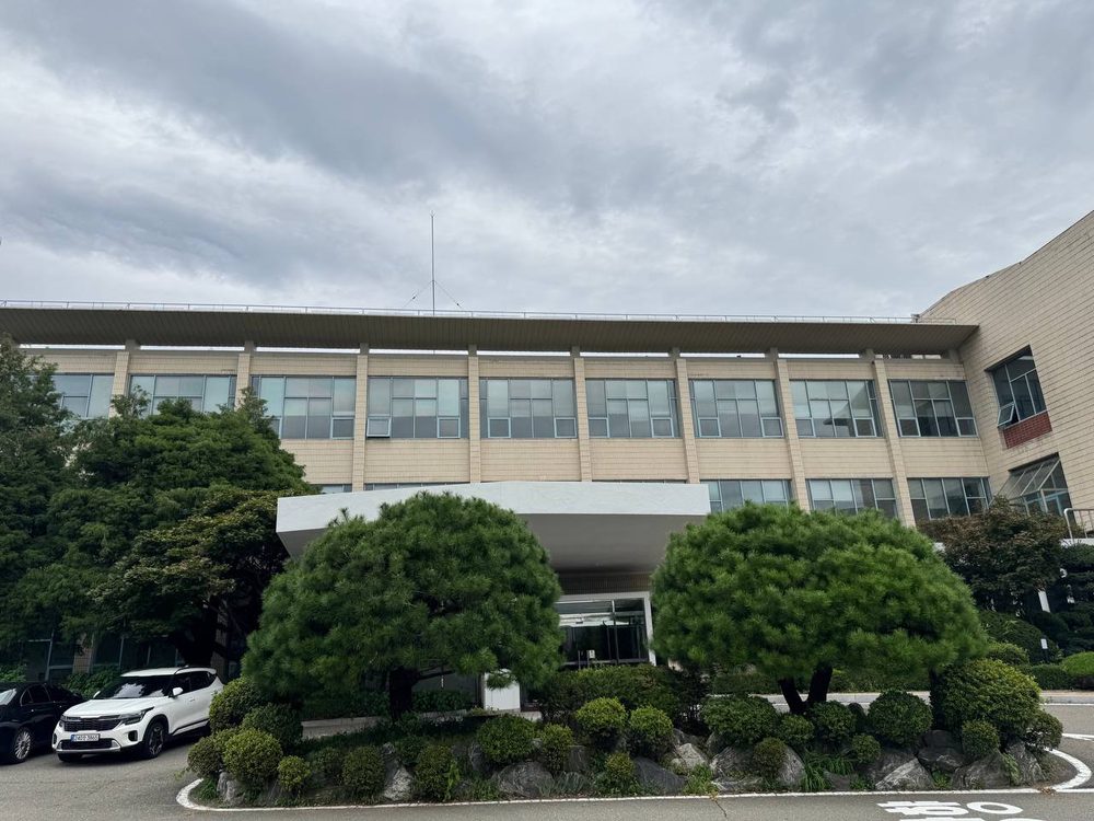 본관 정면의 긴 창과 흰 차양 아래로 소나무 두 그루와 바위로 꾸민 화단이 보인다