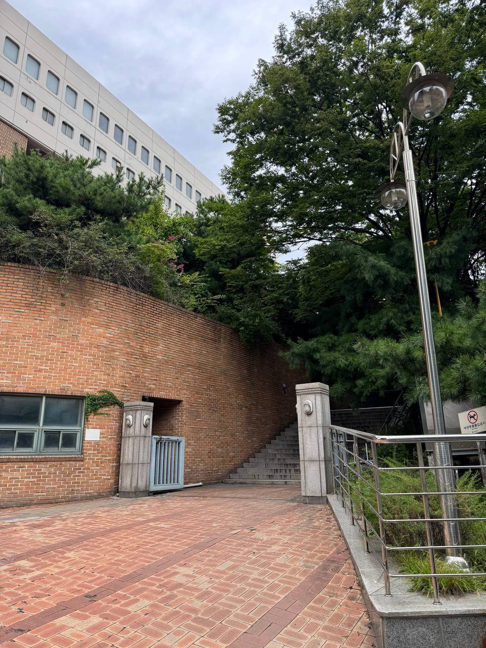 붉은 벽돌 옹벽 아래 넓은 벽돌 광장과 그 옆으로 이어지는 계단, 오른쪽에 둥근 전등이 달린 가로등과 스테인리스 난간이 있다